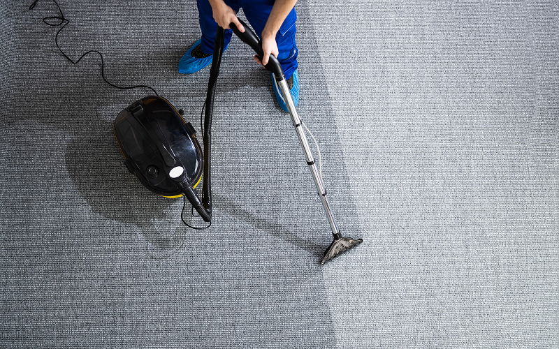 Professional cleaner vacuuming grey office carpet from overhead view.